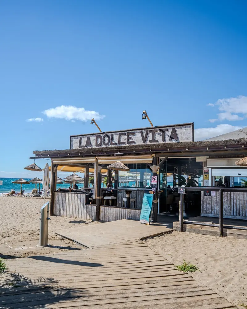 The wooden boardwalk across the sand leading to the La Dolce Vita sign