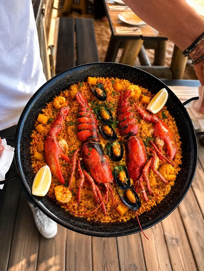 A paella pan of lobster rice with mussels and lemon, held over a wooden table