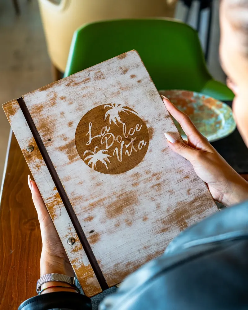 A guest holding the wooden menu cover with the La Dolce Vita logo