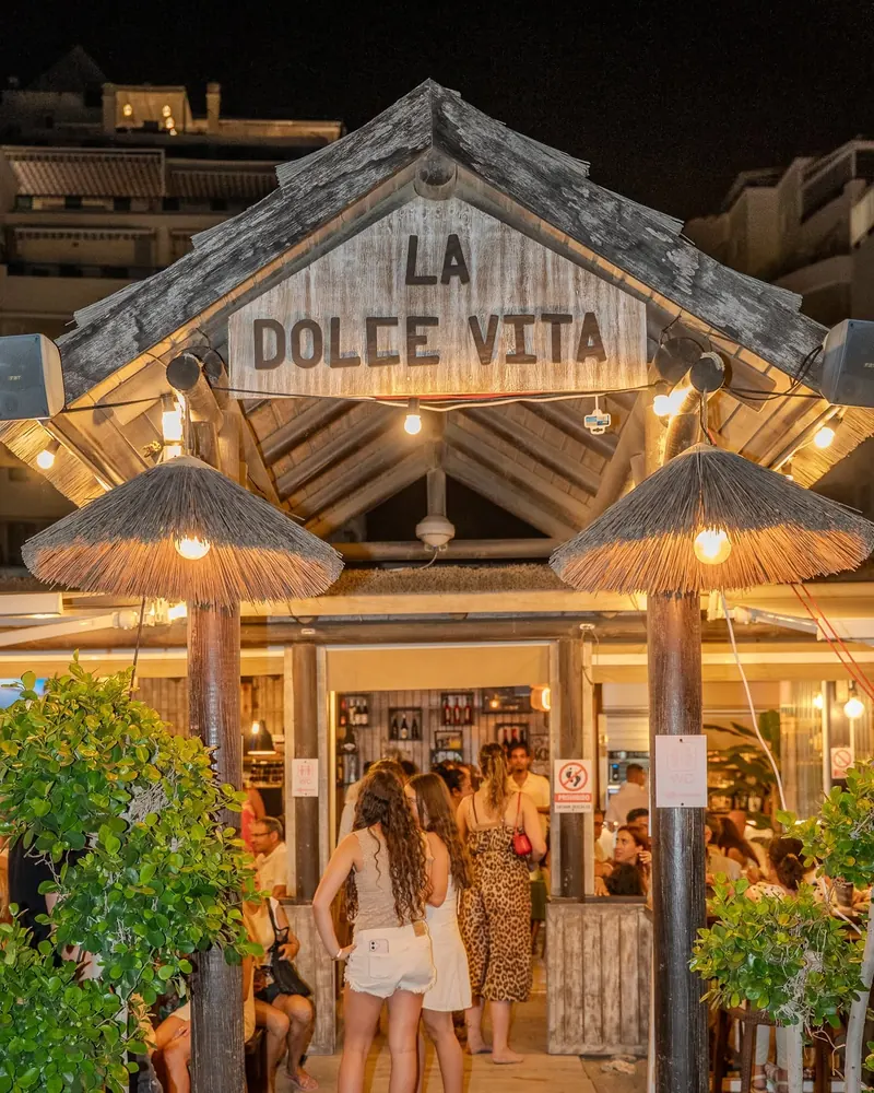 The lit wooden entrance of La Dolce Vita in the evening, with guests arriving