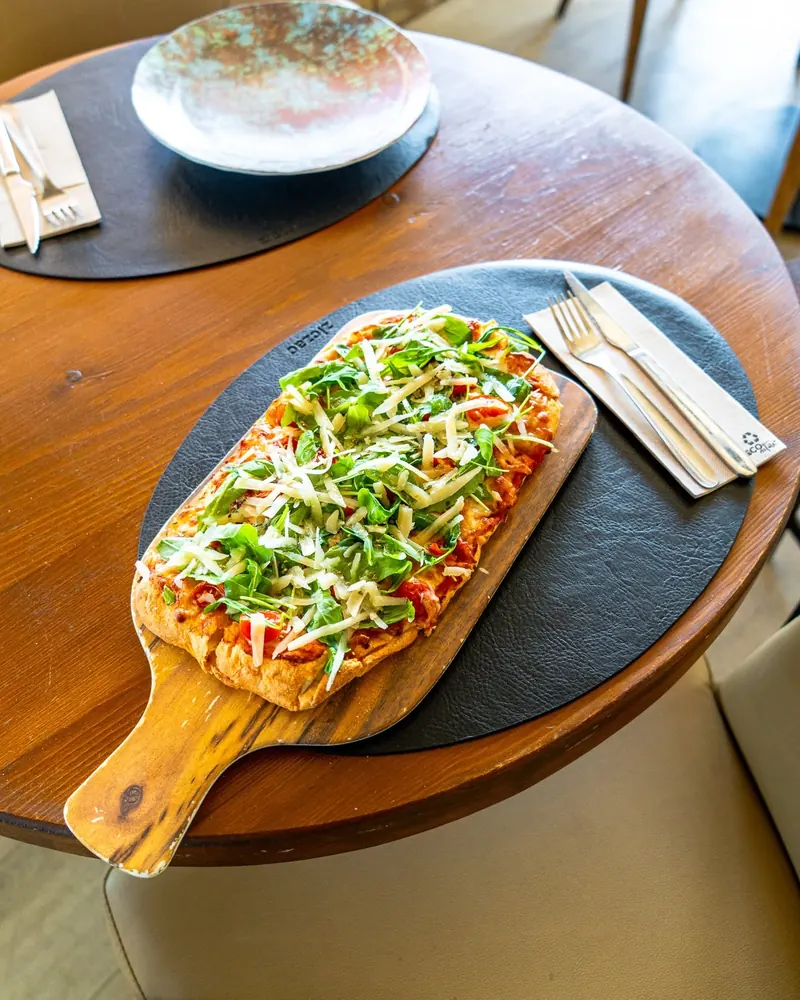 A rectangular pizza topped with rocket and parmesan on a wooden board