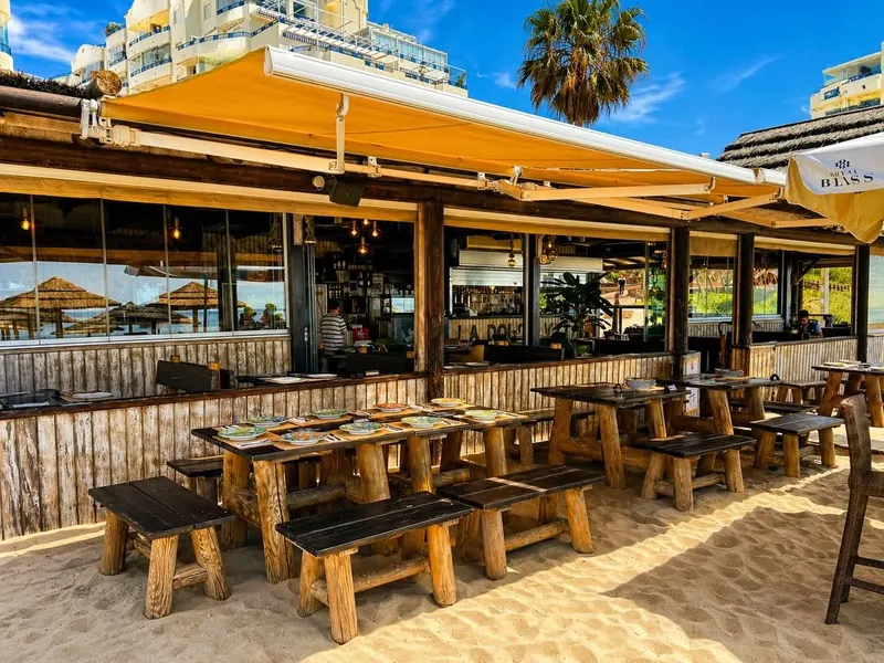 Rustic wooden tables and benches set on the sand in front of the chiringuito