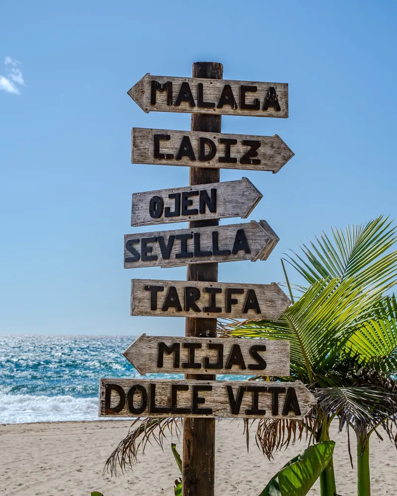 A wooden signpost on the beach pointing to Málaga, Cádiz, Ojén, Sevilla, Tarifa, Mijas and Dolce Vita
