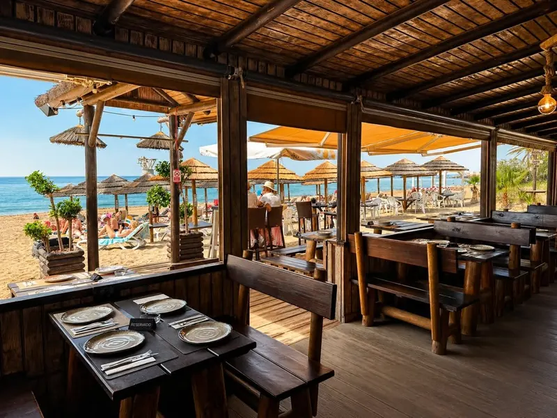 Inside the wooden dining room, with dark timber tables and the beach beyond